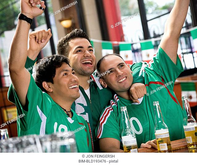 Cheering Hispanic men watching television in sports bar