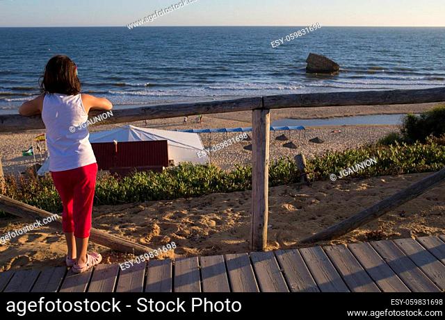 Little girl observing Donana Beach from wooden footpath. Costa de la Luz seashore, Huelva, Spain