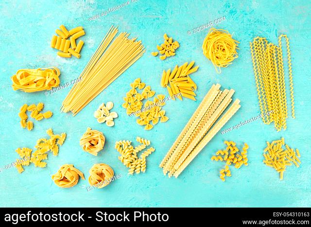 Italian pasta variety, flat lay banner, overhead shot on a blue background. Spaghetti, macaroni, farfalle, penne, pappardelle etc