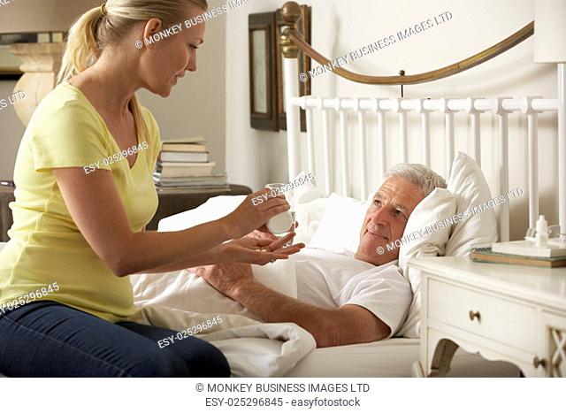 Adult Daughter Giving Senior Male Parent Medication In Bed At Home