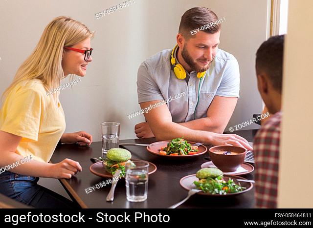 Picture of business people looking at laptop computer's screen and smiling while sitting in vegan restaurant or cafe