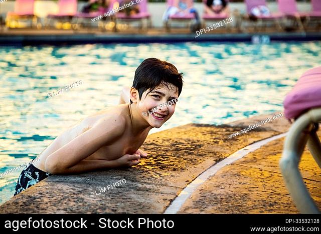 Portrait of a boy leaning on the edge of a swimming pool at a resort in Ka'anapali and poses for the camera; Ka'anapali, Maui, Hawaii, United States of America