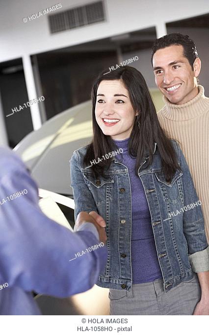Couple shaking hands with a car salesperson