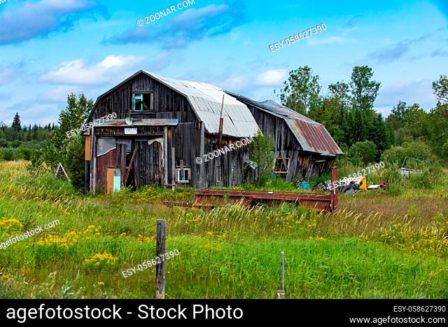 A wide angle view of a dilapidated farm building. Neglected wood barn in a state of disrepair surrounded by rural farmland, with copy space to right