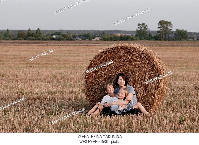 Woman with two kids sitting near a haystack on a stubble field