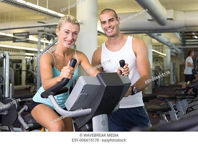 Male trainer assisting woman with exercise bike at gym