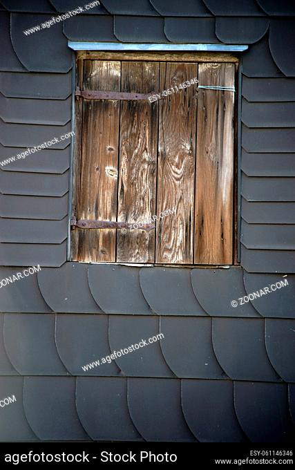Eine markante Dachluke aus Holz an einer Fassade aus Schieferschindeln