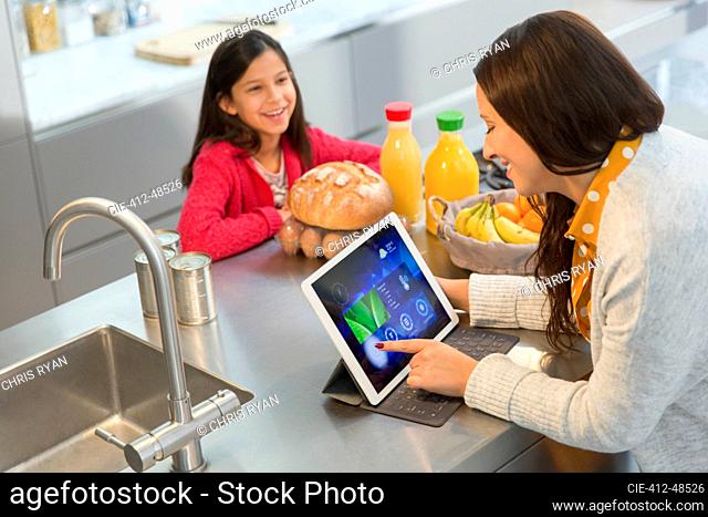 Daughter watching mother using digital tablet in kitchen