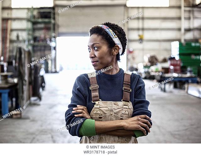 Black woman factory worker wearing coveralls in a large sheet metal factory