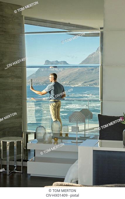 Reflection of man using digital tablet camera on luxury balcony with ocean view