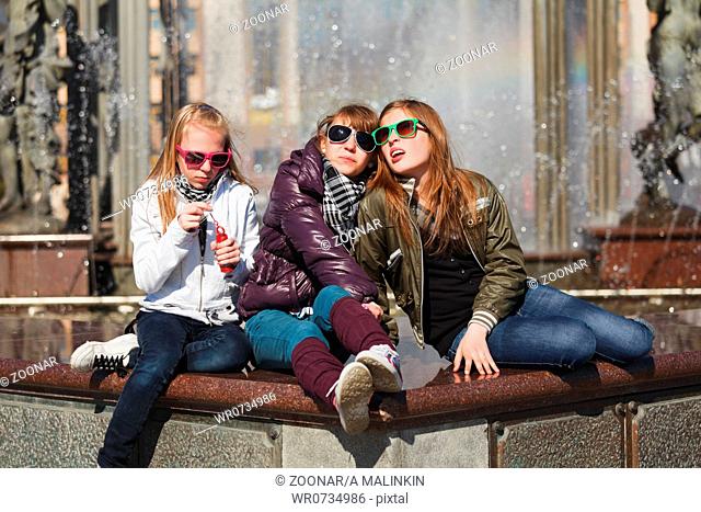 Teenage girls relaxing against a city fountain