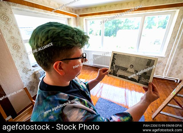 PRODUCTION - 08 June 2023, Lower Saxony, Rosengarten: A staff member shows an old photo of the Matz family taken in this living room of the original refugee...