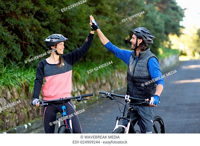 Biker couple giving high five while riding bicycle on the road