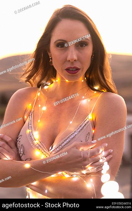 A gorgeous Hispanic Brunette model poses outdoors at sunset with small lights