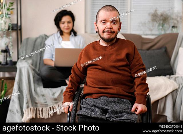 Smiling man in wheelchair in front of girlfriend with laptop at home