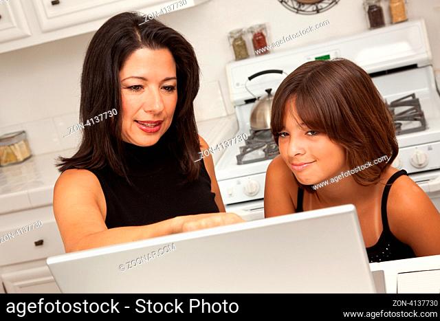 Attractive Hispanic Mother and Mixed Race Daughter in the Kitchen using the Laptop Computer Together