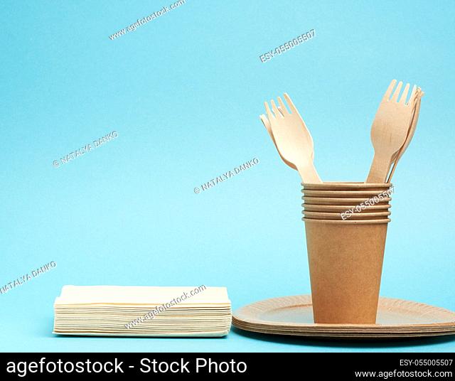 paper cup, plates from brown craft paper and wooden forks and knives on a blue background. Plastic rejection concept, zero waste