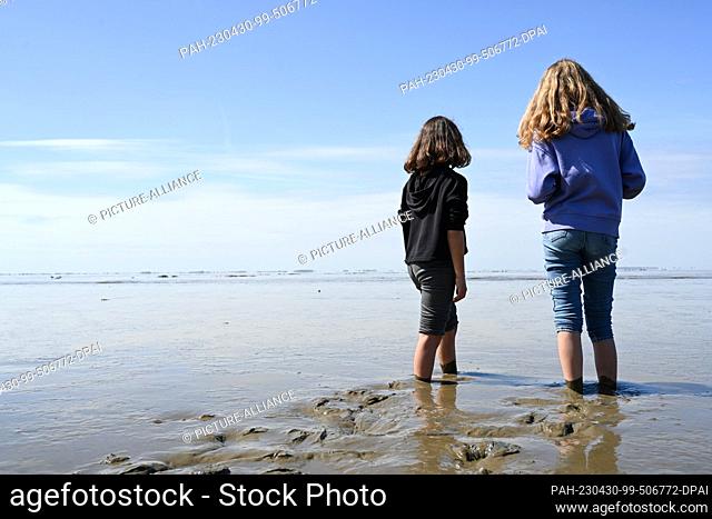30 April 2023, Lower Saxony, Ditzum: Two girls are barefoot in the Wadden Sea and enjoy the weather. Photo: Lars Klemmer/dpa