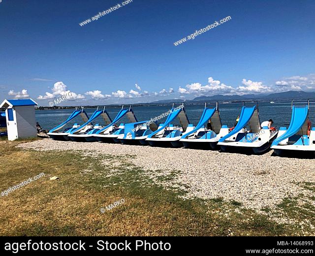 pedal boats and houses in blue and white on the beach of lake garda, peschiera del garda, veneto, verona, italy