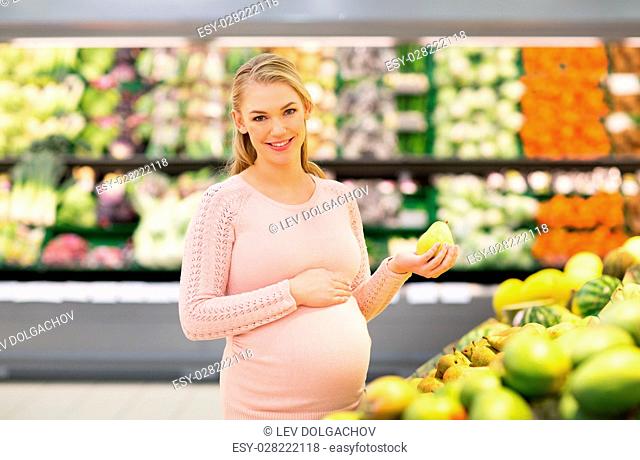 sale, shopping, food, pregnancy and people concept - happy pregnant woman with pear at grocery store or supermarket