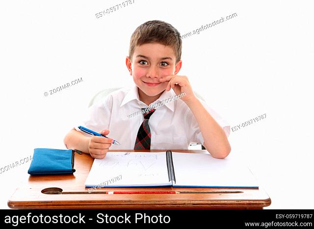 A happy young school student 6 year old boy sitting at school desk and smiling