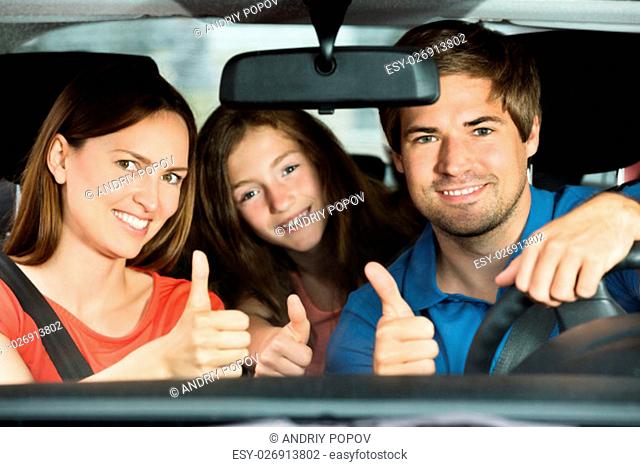 Happy Young Couple Driving In Car With Their Daughter