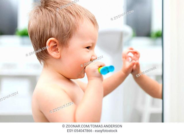 Adorable child learing how to brush his teeth in the bathroom