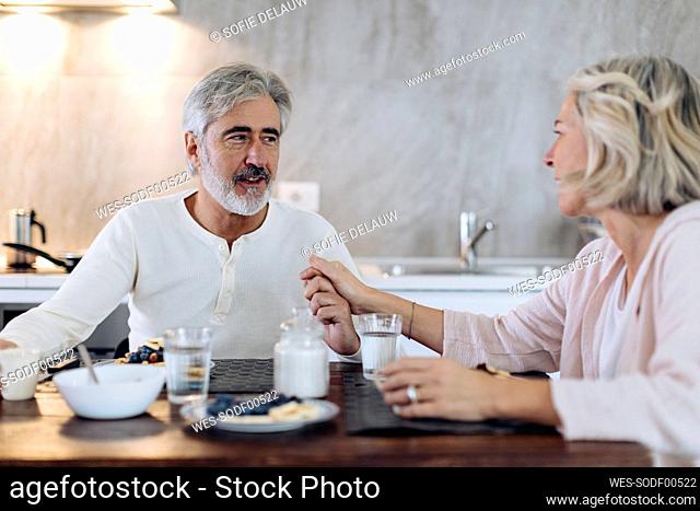 Affectionate mature couple sitting at table in kitchen at home having breakfast