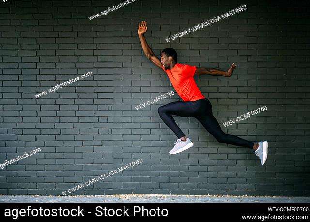 Young sportive man jumping in front of a brick wall