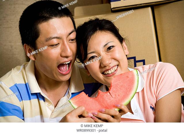 Couple sharing watermelon and smiling with cardboard boxes in background