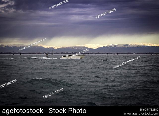 View of Venice Lagoon with dramatic overcast stormy sky and horizon in the distance sunlit peaks of Dolomite Alps, Venice, Italy