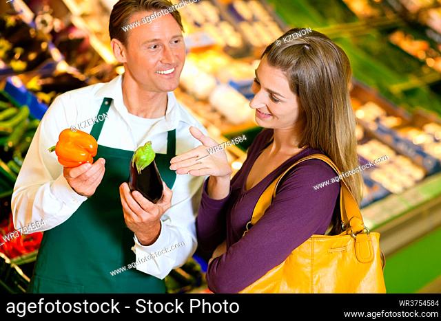 woman in a supermarket at the vegetable shelf shopping for groceries, a shop assistant is helping her