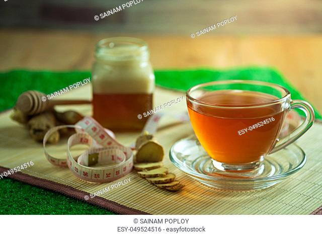 Ginger juice in a clear cup and honey jar placed beside with measuring tape. Concept of healthy