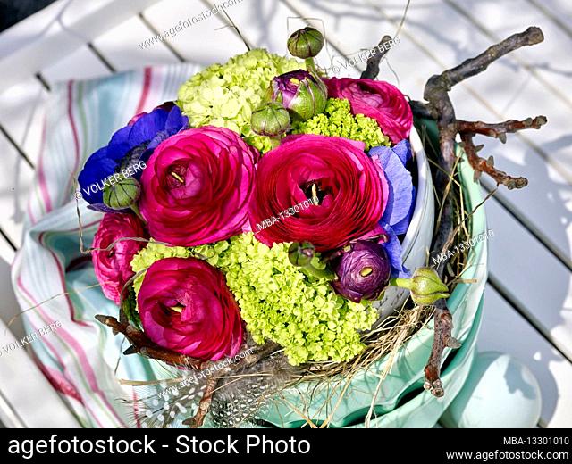 Easter bouquet made of anemones and ranunculus in a green earthenware bowl with Easter eggs on a white tea trolley