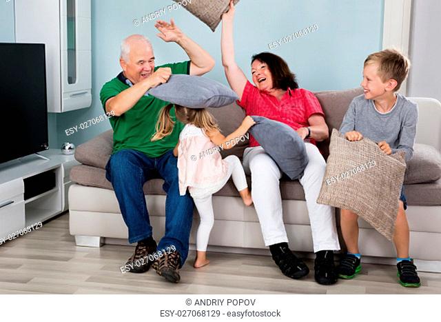 Grandparent And Kids Having Pillow Fight While Sitting On Couch Together At Home