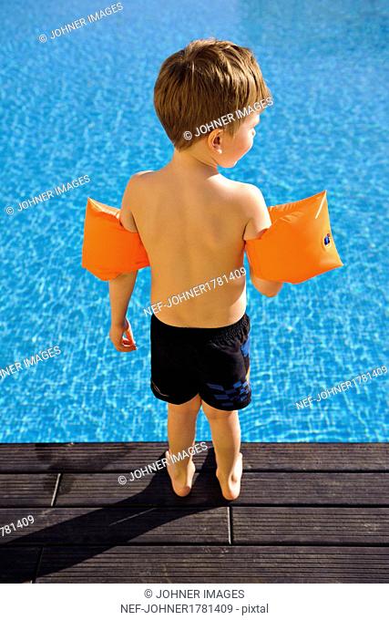 Boy wearing inflatable armbands on edge of swimming-pool