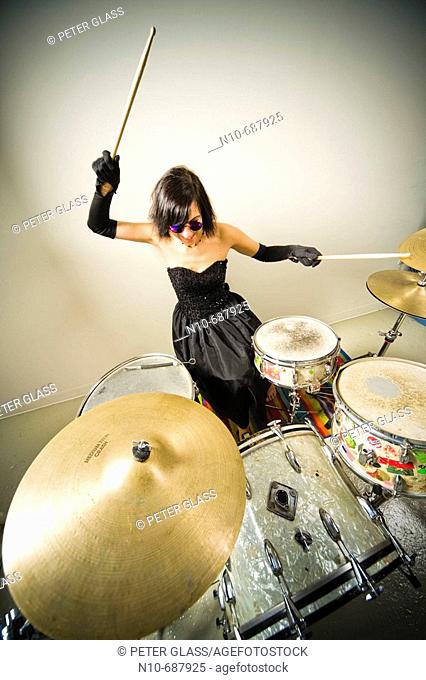 Woman, wearing an evening gown and blue sunglasses, playing the drums