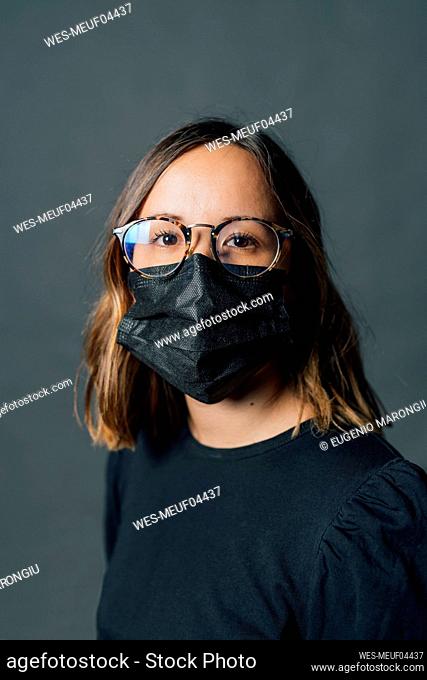 Young woman wearing black protective face mask against gray background