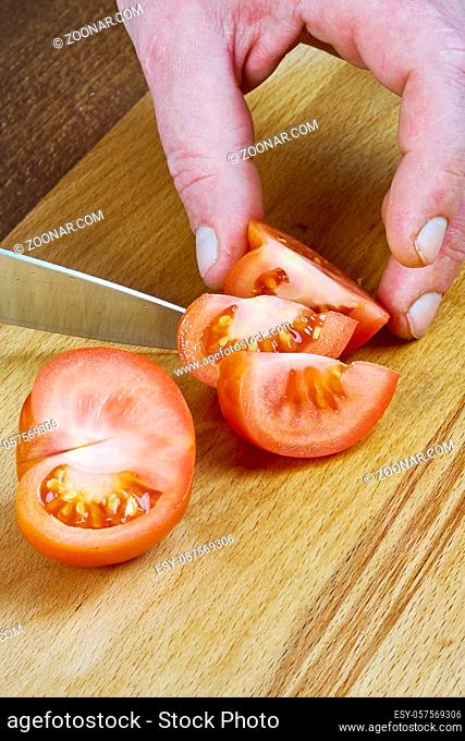 cook cuts a tomato on a wooden board Food being prepared and cooked in a contemporary kitchen, with and without the chef
