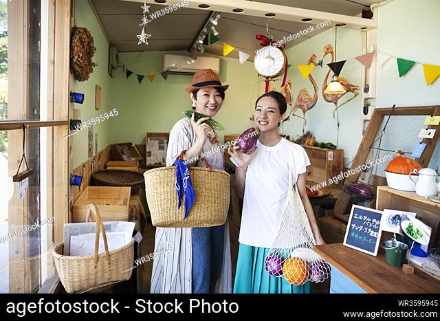 Two smiling Japanese women standing in a farm shop, looking at camera