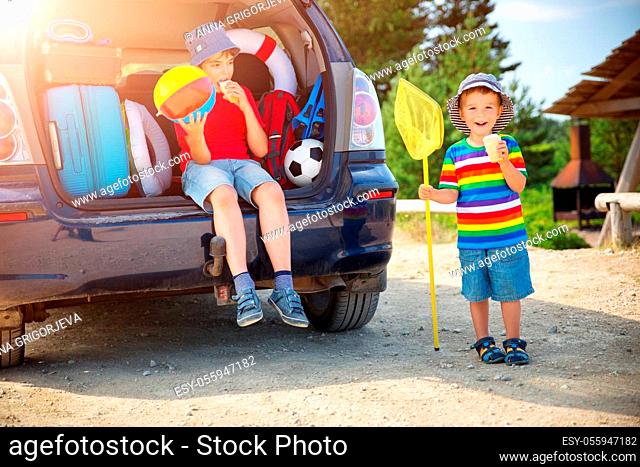 Boy resting in nature in beautiful summer day. child sitting in car filled with traveling accessories and luggage. Travel and vacations concept