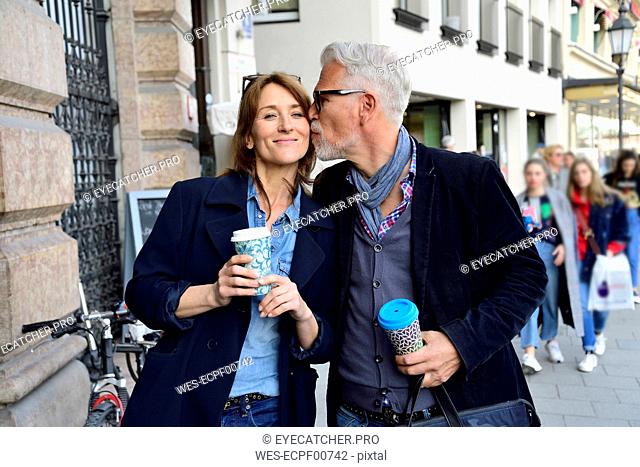 Mature couple with reusable bamboo cups kissing in the city
