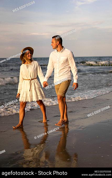 Boyfriend and girlfriend holding hands while walking at beach on sunset