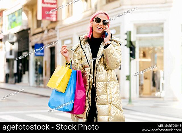 Young fashionable woman with shopping bags talking on mobile phone while standing in city