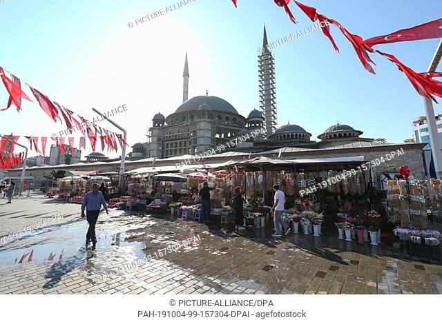 03 October 2019, Turkey, Istanbul: A scaffolded minaret stands in the city centre at a mosque. In the foreground traders have built flowers at a market