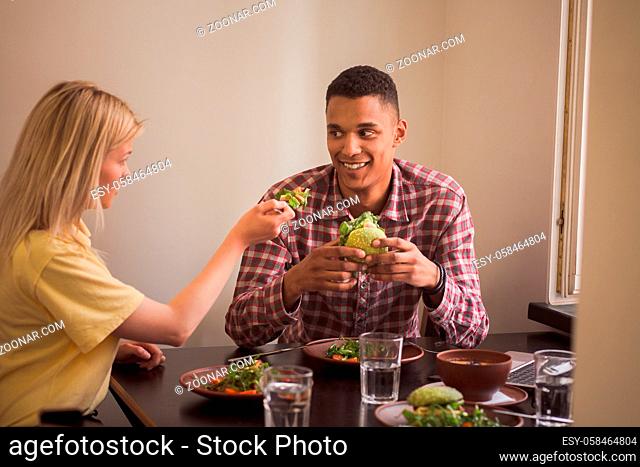 People looking at each other while sitting at table. Happy couple eating vegan dishes in vegan restaurant or cafe