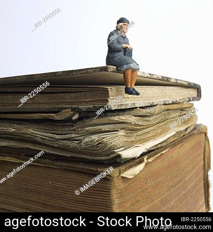 Elderly lady, miniature figurine, sitting on an old book