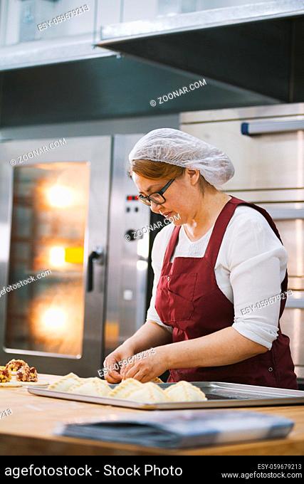 Adult woman in glasses and apron bakes cakes with her hands in the bakery