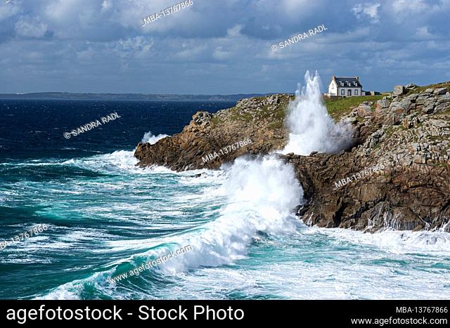 Waves crash on the rocky coast at Pointe du Millier, house and lighthouse Phare du Millier on the cliffs, France, Brittany, Finistère department, Cap Sizun
