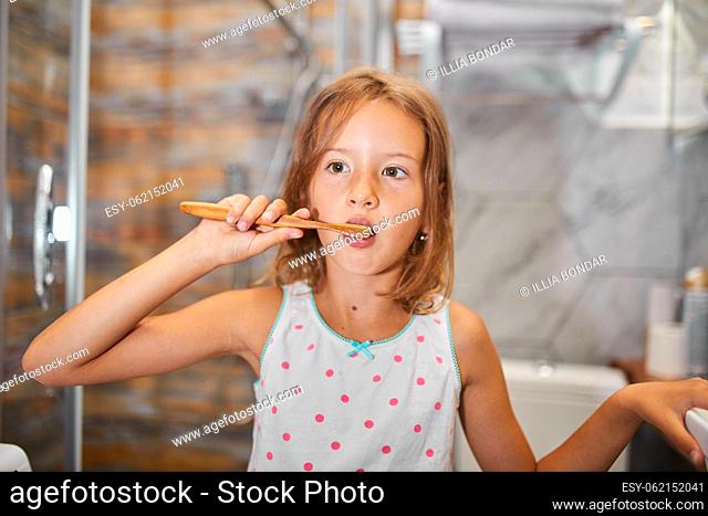 Little Girl brushing teeth with ecologe wooden Toothbrush in the bathroom at home, healthy hygiene concept